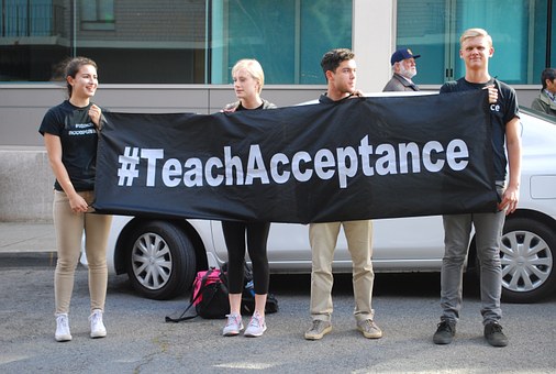 Four young adults holding a "#TeachAcceptance" banner to promote acceptance of others